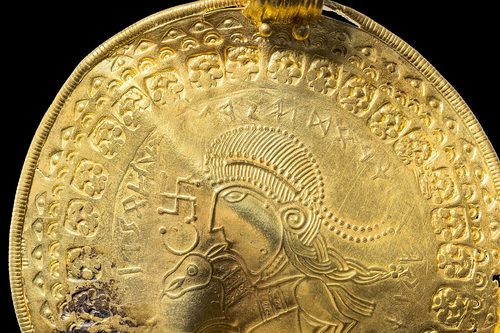 Detail of Vindelev bracteate X13: a head with a long braid above a horse, with the runic inscription read as "He is Odin's man". National Museum of Denmark photograph.